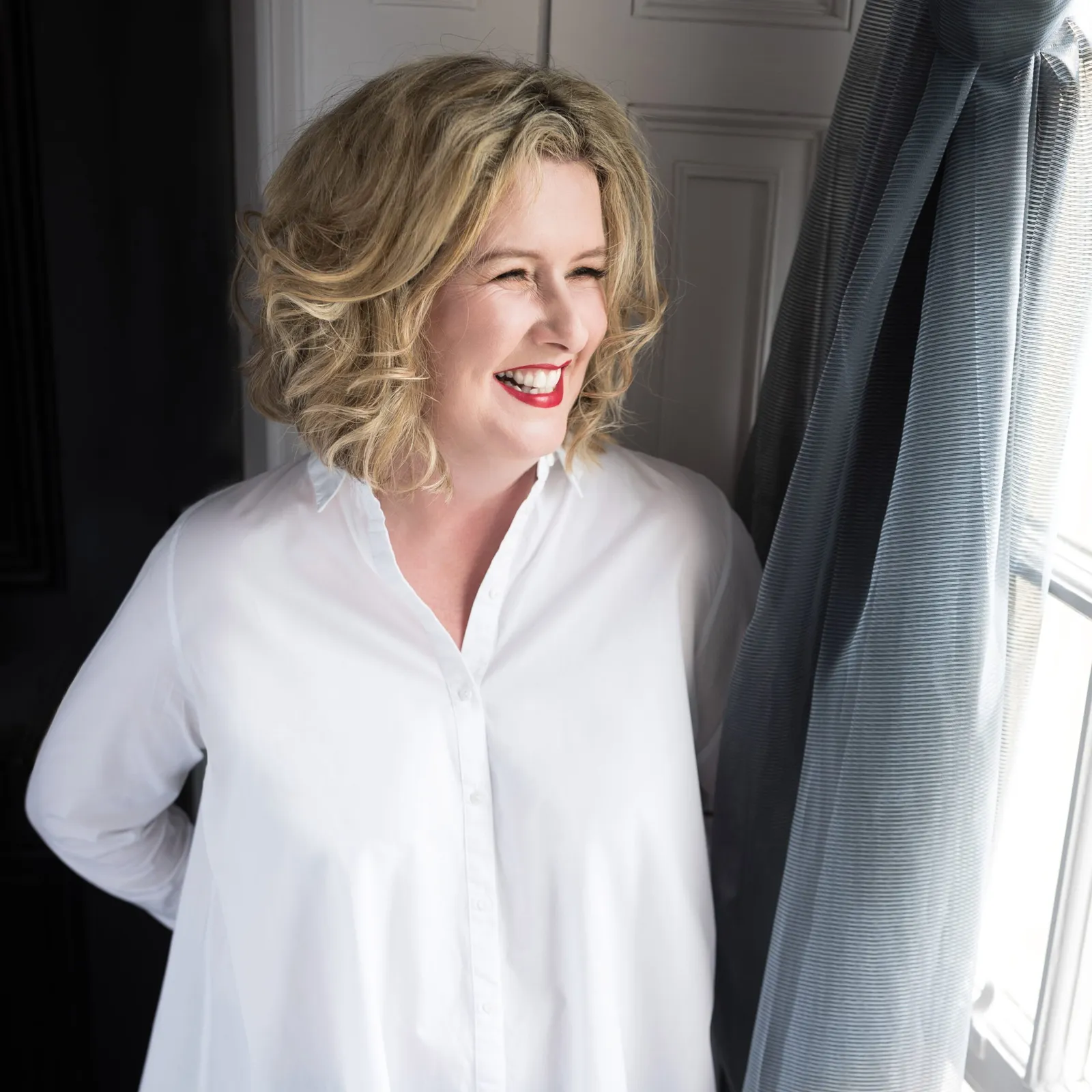 1:1 Square profile photo of Helen Hogben in a white blouse standing next to a sash window at Acklam Hall in Middlesbrough, North Yorkshire.
